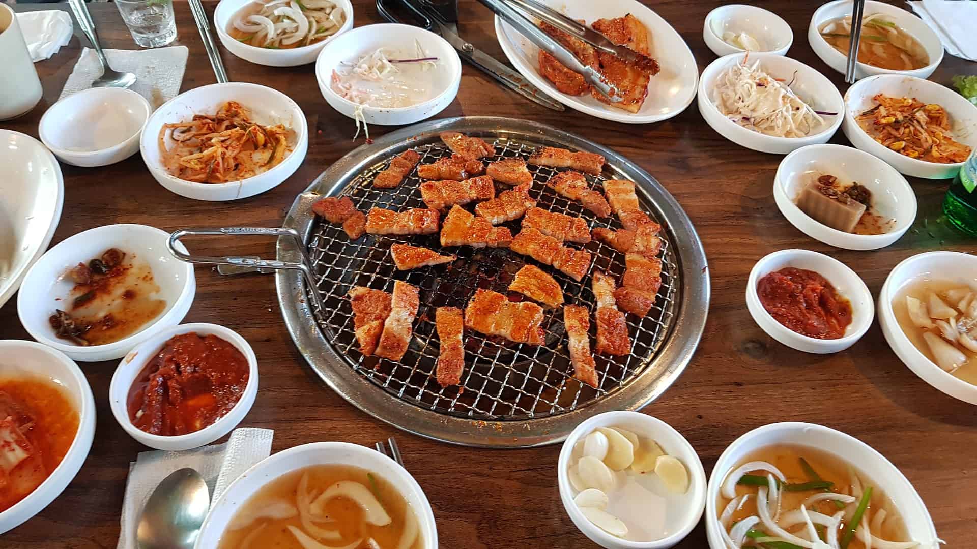 मध्यभागी ग्रील्ड मांस अनेक कोरियन पदार्थांनी वेढलेले