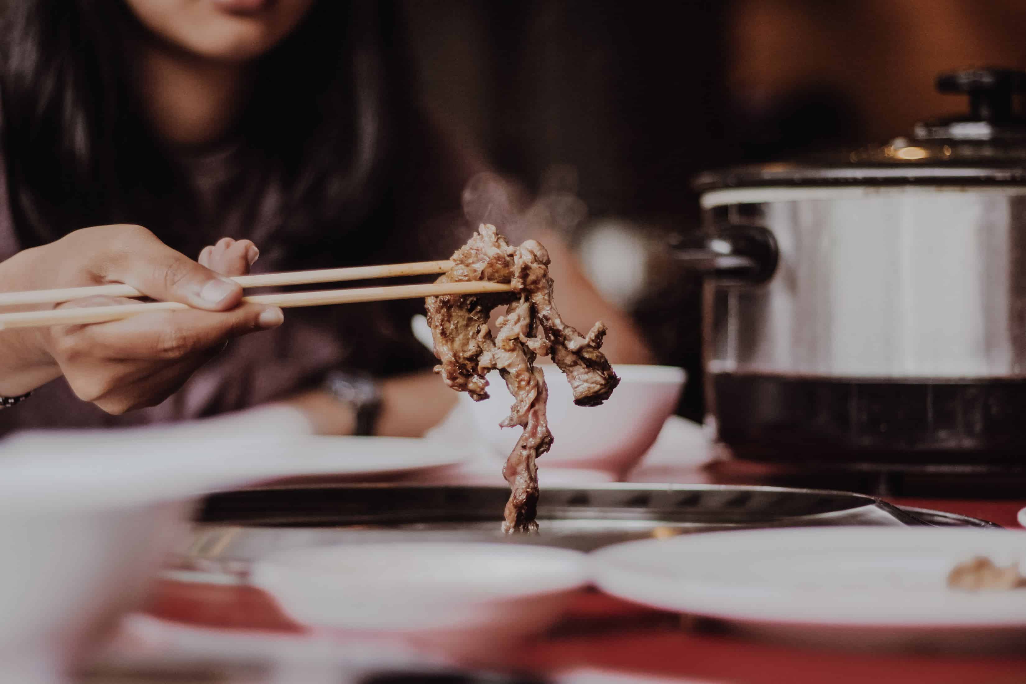 uma pessoa está comendo yakiniku com pauzinhos