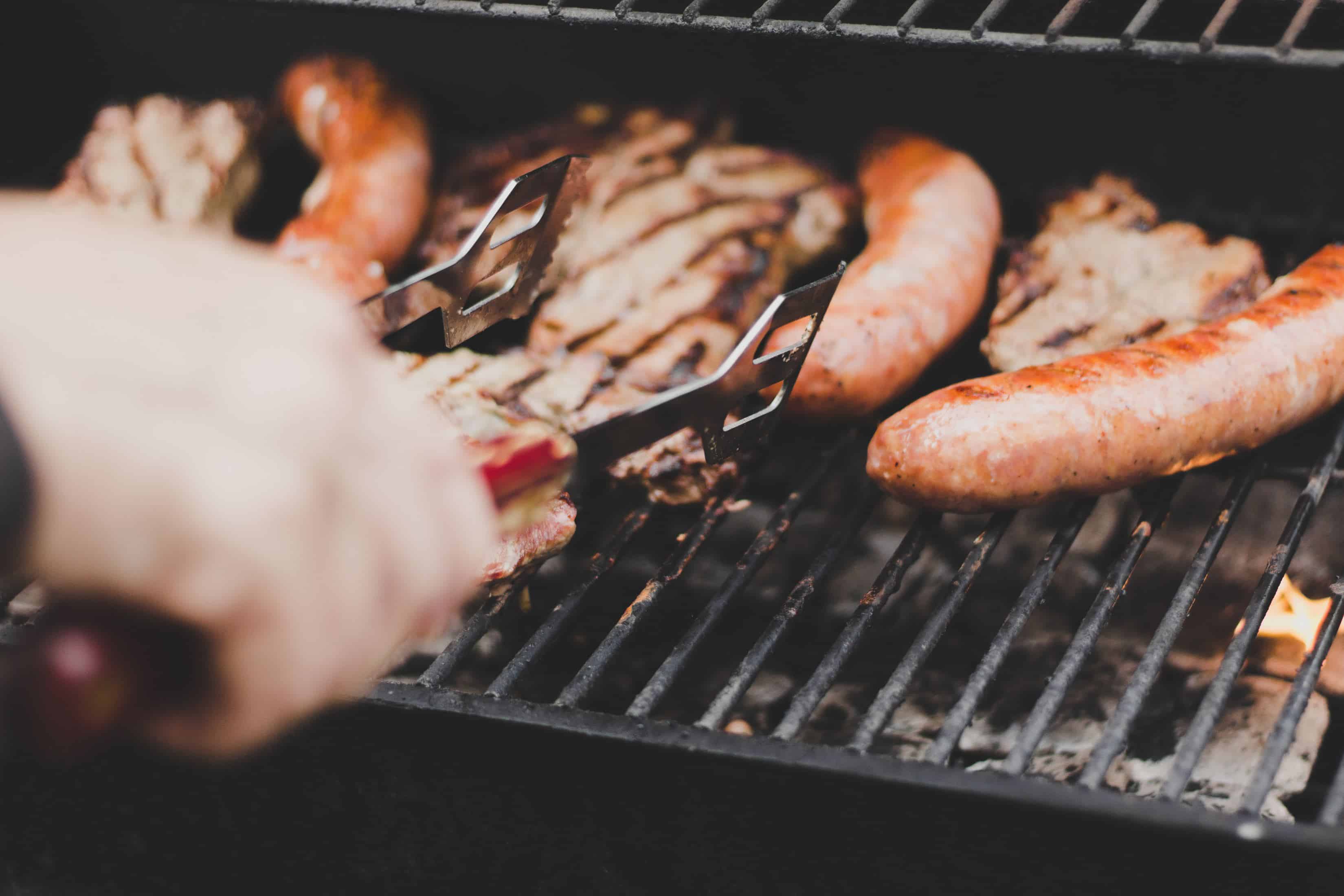 someone is grilling meat and sausages with a tong