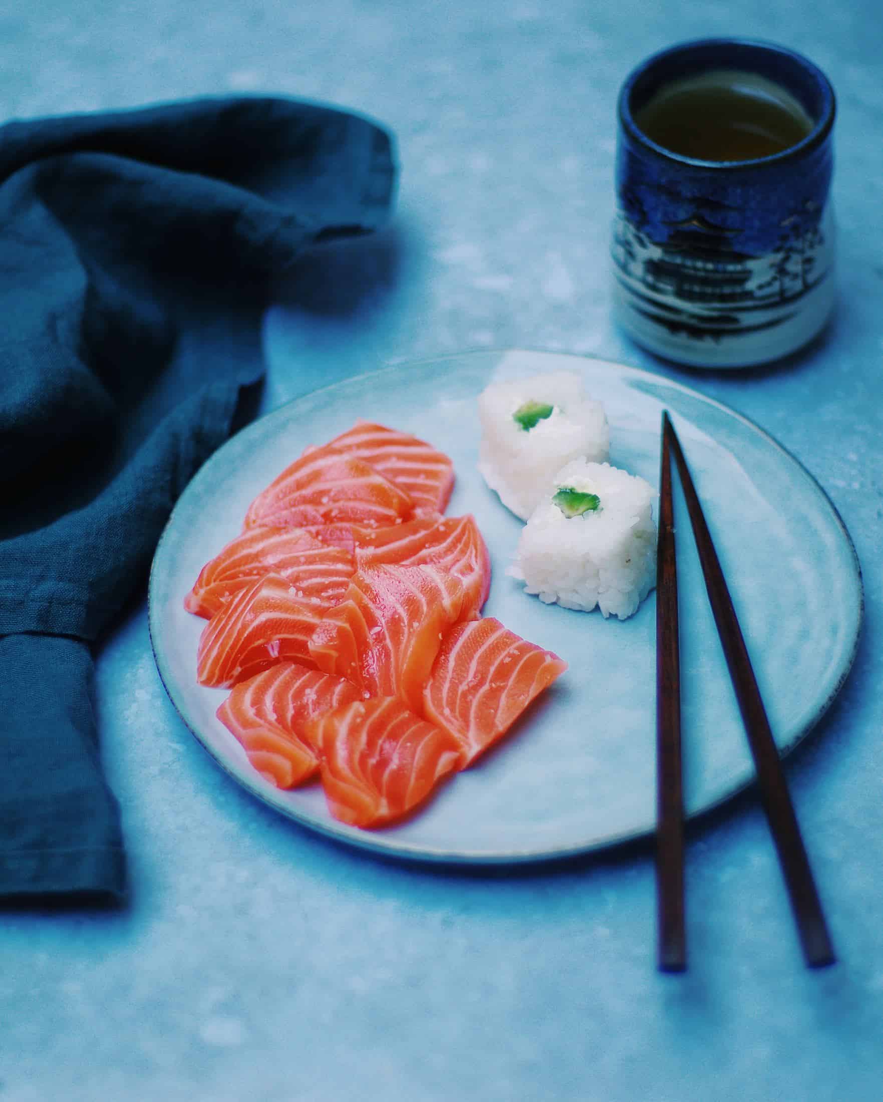a plate of sashimi and sushi, and a glass of hot tea