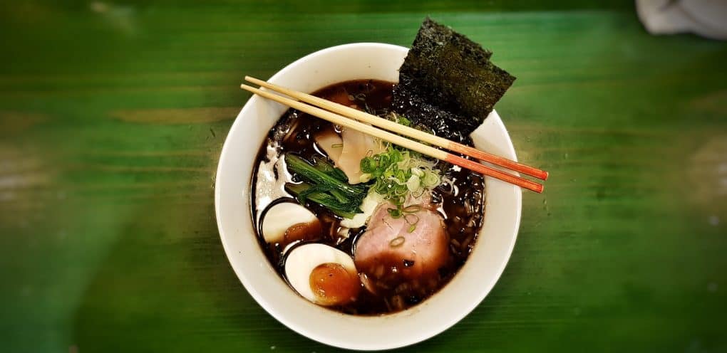 uma tigela de ramen contendo ovos, carne, algas marinhas, com uma sopa de cor preta