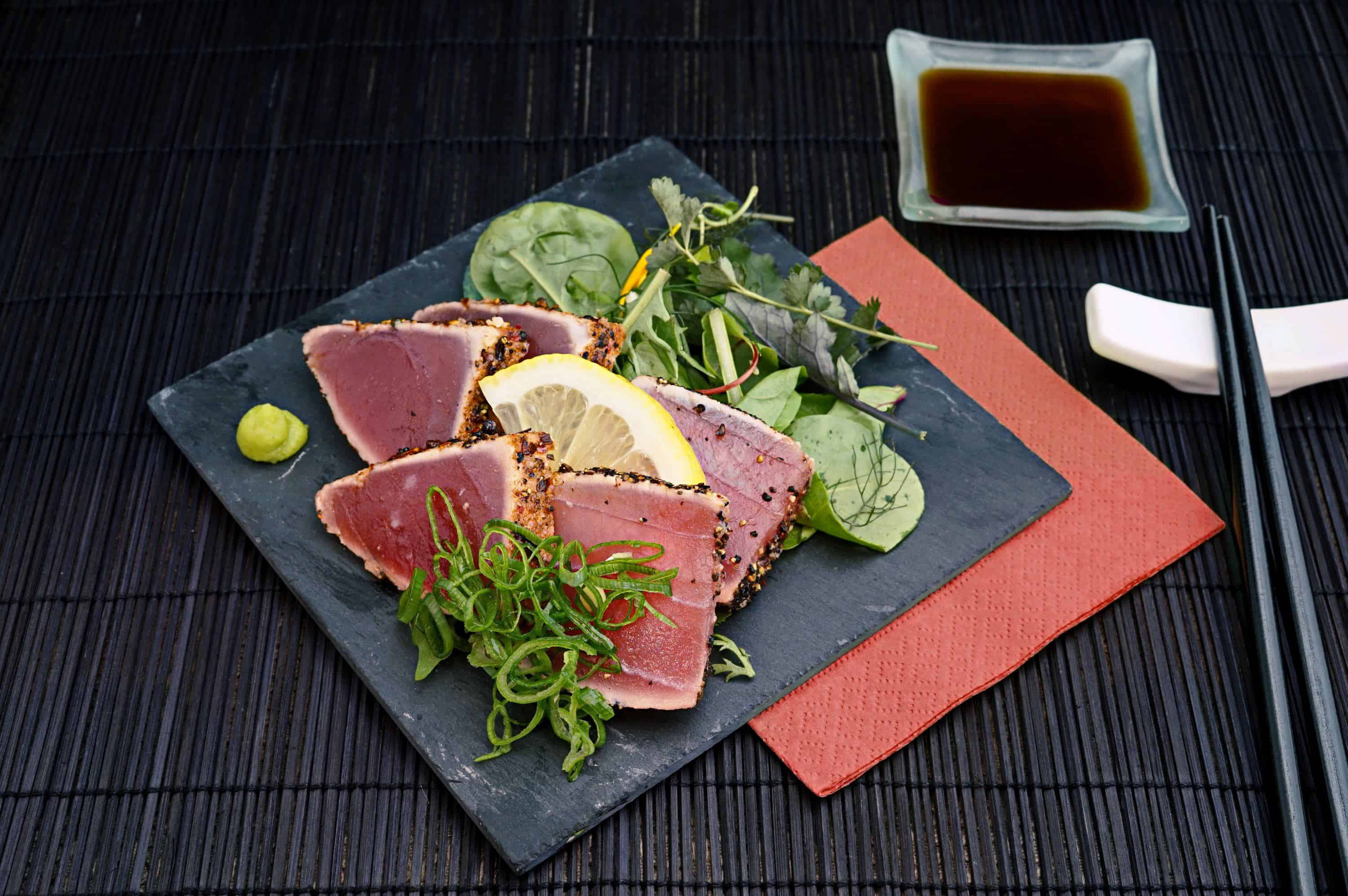 un plato de sashimi y verduras con salsa de soja y palillos al lado