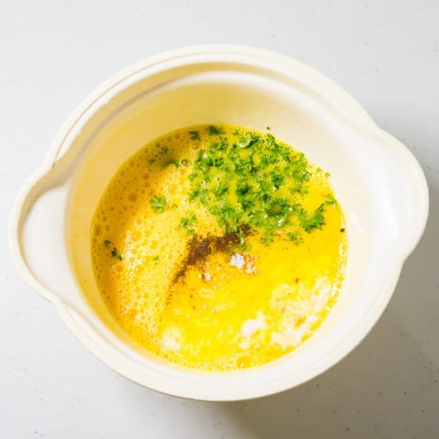Omelettägg i en skål med persilja och senapspulver