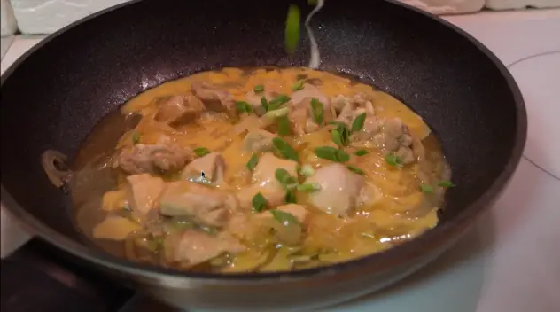 Adding cut green onion to the oyakodon in the skillet