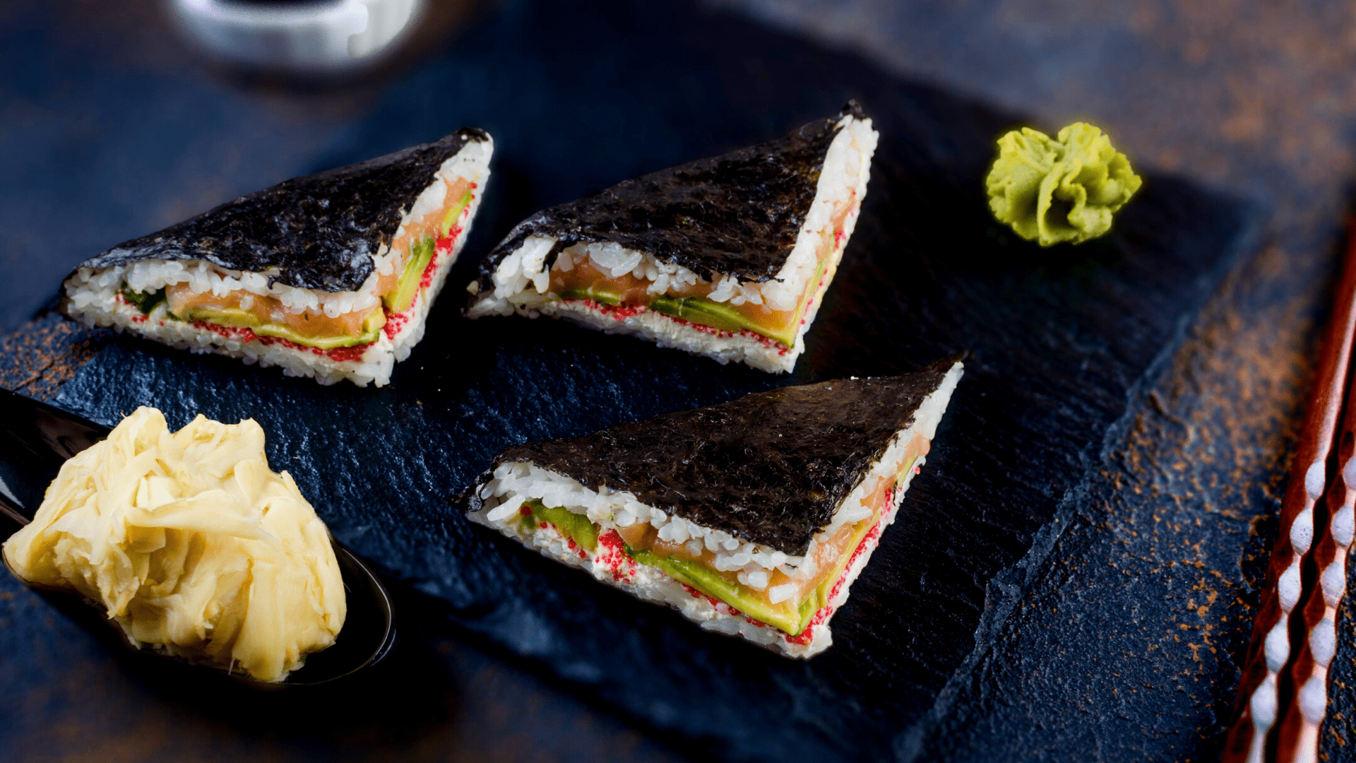 3 triangular halves of onigirazu sushi sandwich halves on a plate with wasabi and ginger