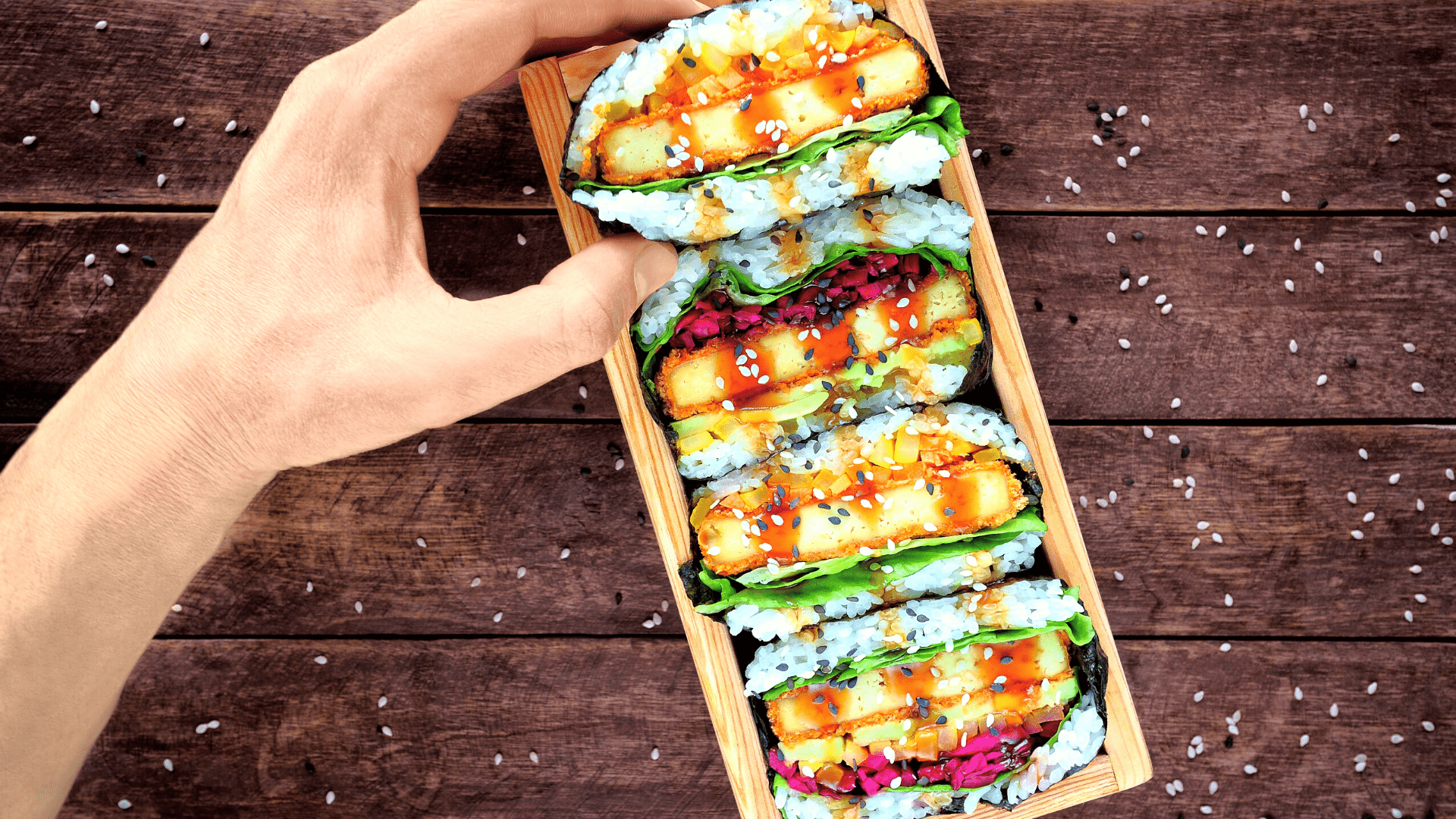 hand holding box of 4 onigirazu sushi sandwich halves