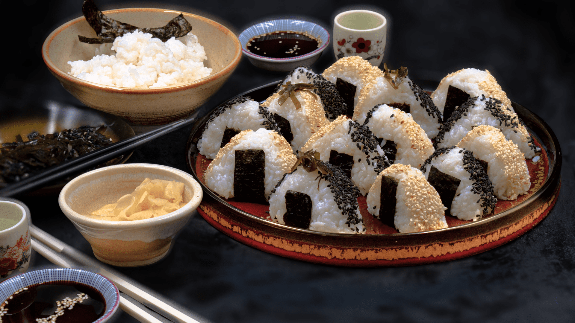 plate of triangle onigiri with bowl of rice, ginger, and soy sauce