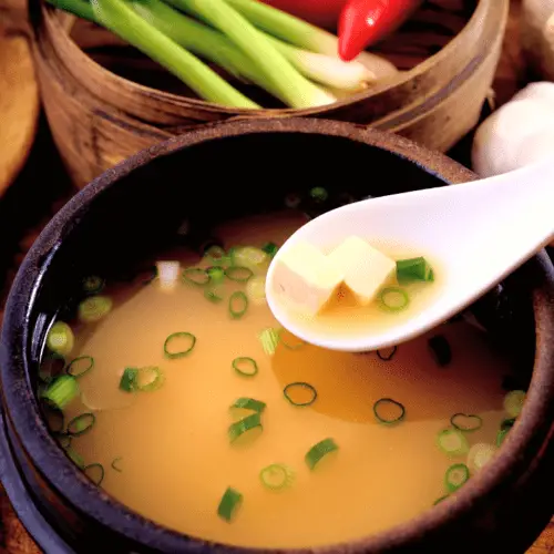 tazón de sopa de miso saikyo con cebollas verdes y tofu con un tazón de cebollas verdes y chiles al lado