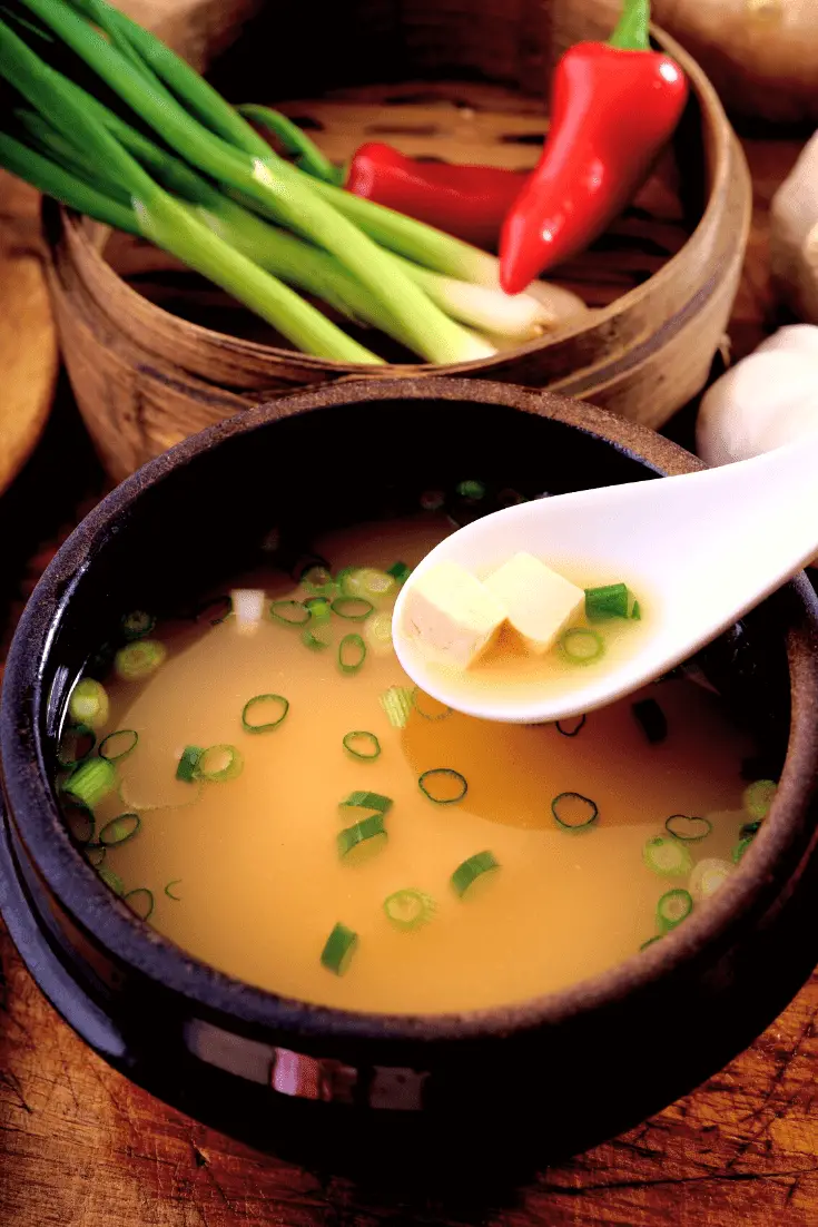 bowl of saikyo miso soup with green onions and tofu with bowl of green onions and chili peppers next to it