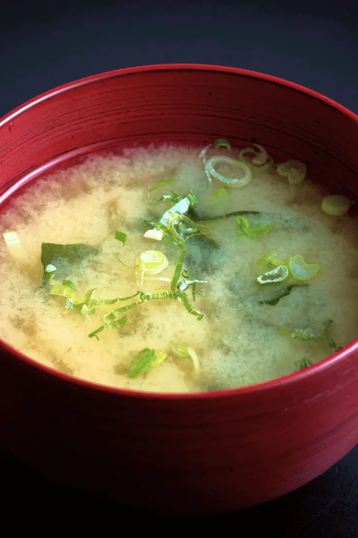 red bowl with white miso soup with seaweed and green onions