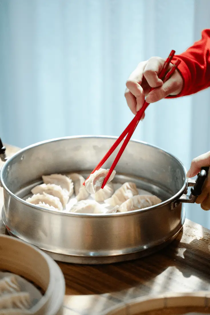 person flipping gyoza in a steamer with chopsticks