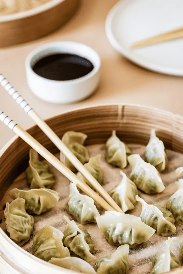 gyoza mewn stemar bambŵ gyda chopsticks a saws soi ar yr ochr