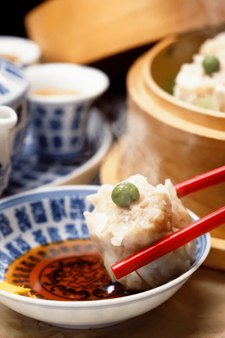 shumai gyda phys ar ei ben, wedi'i ddal gan chopsticks dros ddysgl saws soi