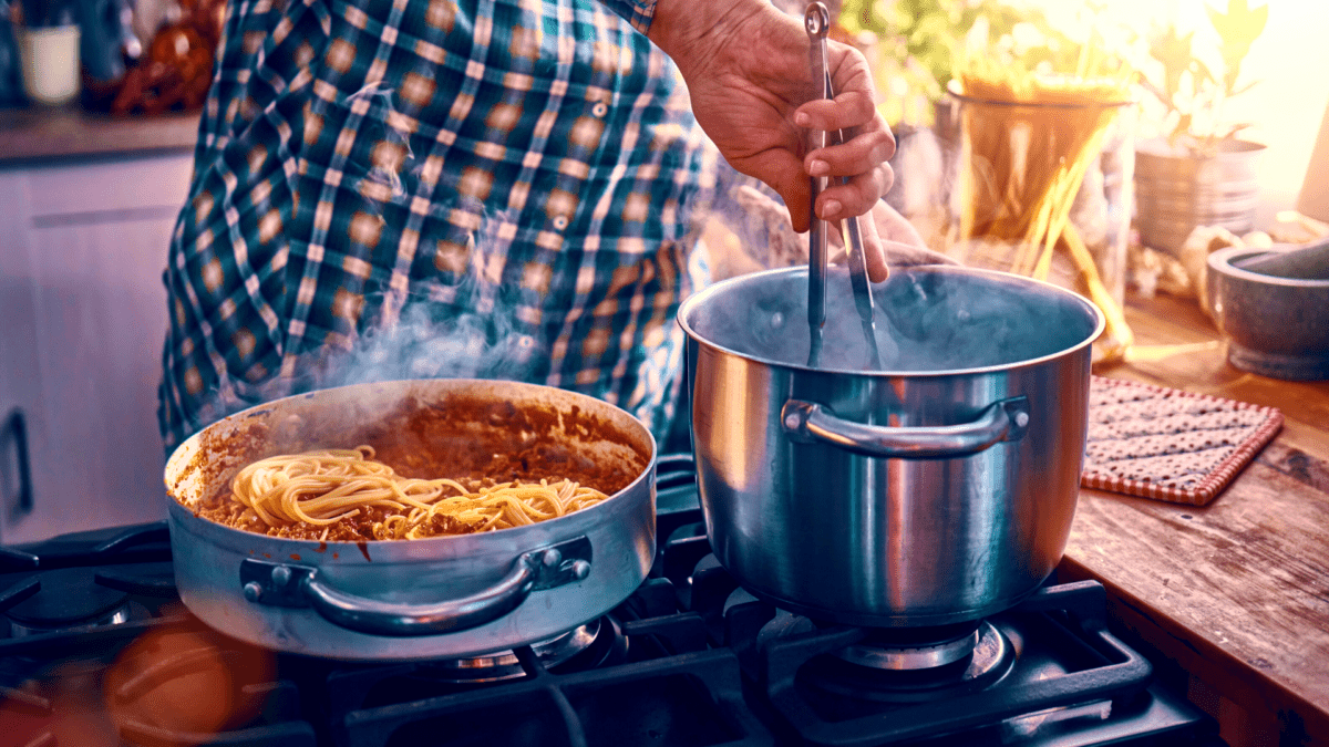 person in checkered shirt cooking Filipino spaghetti over the stove