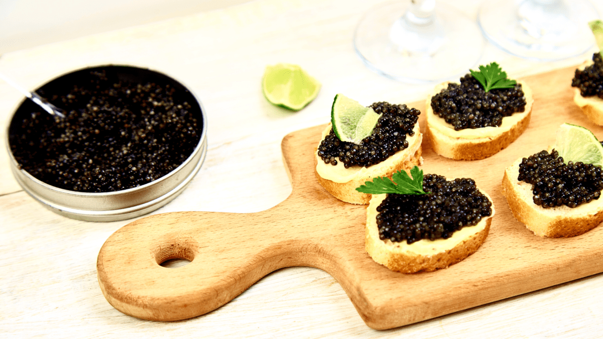 svart klumpfiskkaviar på bröd på en bräda med en skål med kaviar bredvid