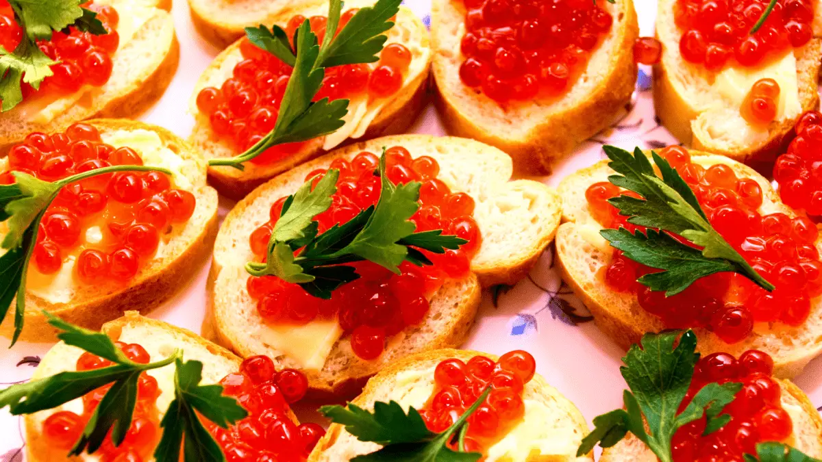 caviar brithyll ar ddarnau o fara gyda garnais perlysiau ar ei ben