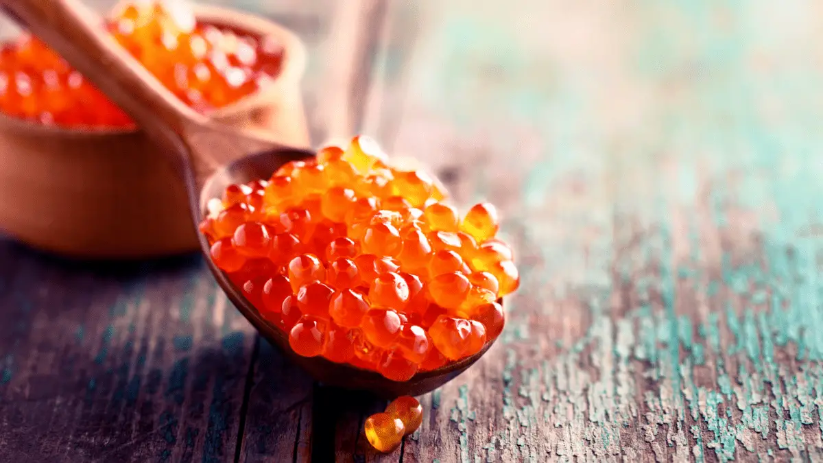 wooden spoon with whitefish caviar and wooden bowl of caviar in the background