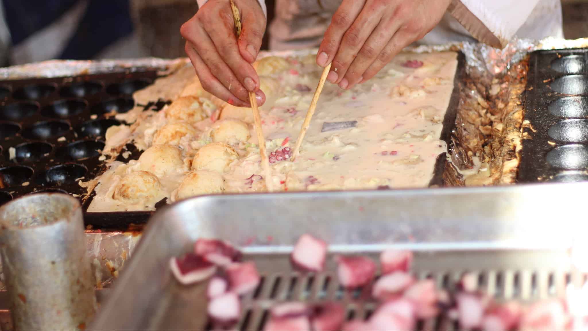 Person adding 1 larger piece of octopus to takoyaki balls