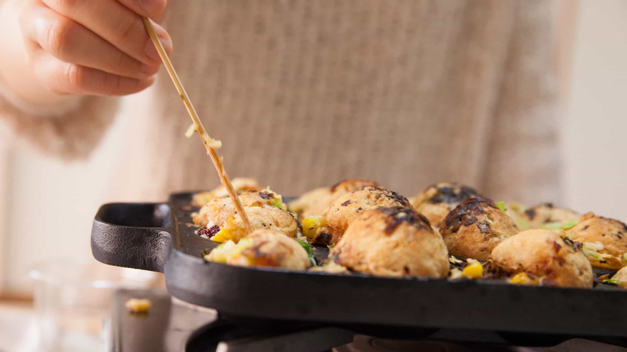 Person sticking pick in the side of a takoyaki ball to flip it