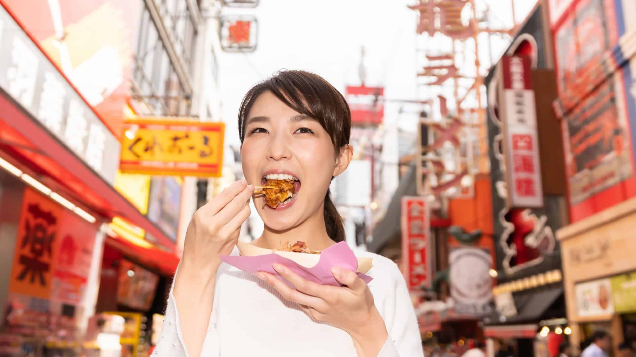 Kvinna som äter takoyaki med en tandpetare